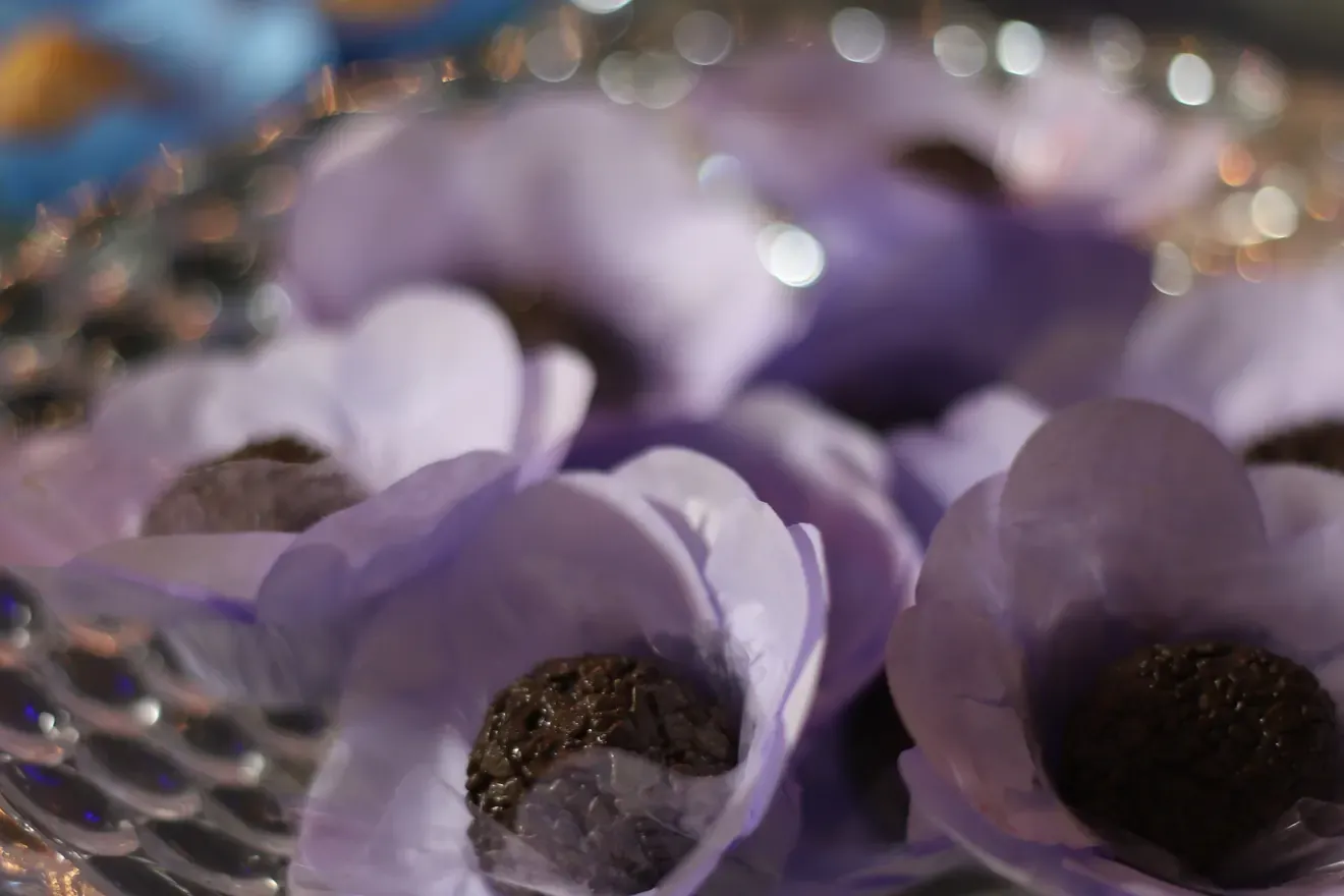 Arranjo de forminhas lilás com brigadeiros sobre suporte de cristal numa mesa de festa