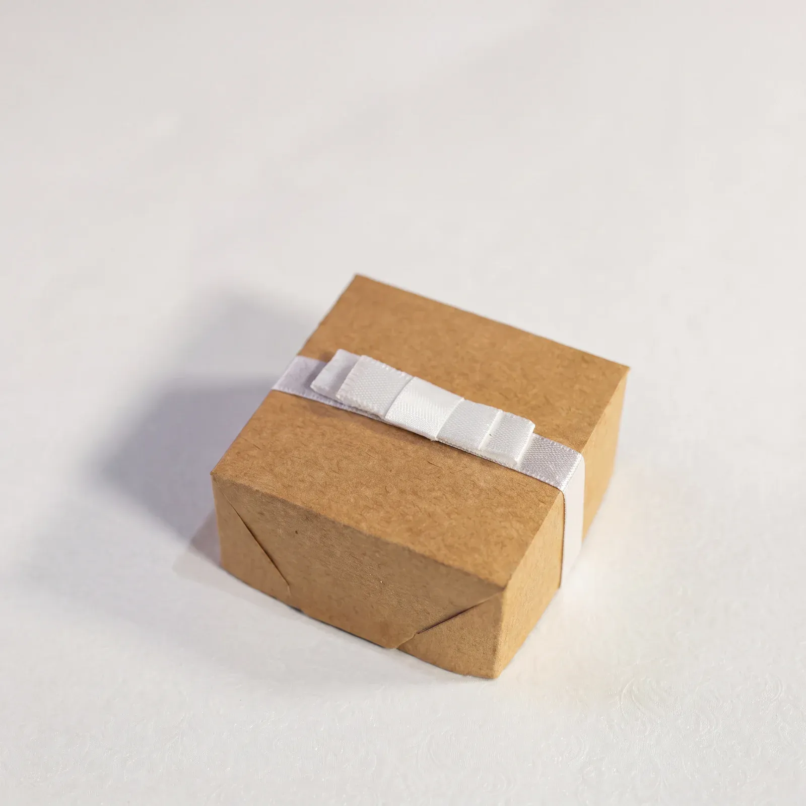 Caixa de papel kraft da Embalarte fechada com laço de cetim branco, sobre fundo claro