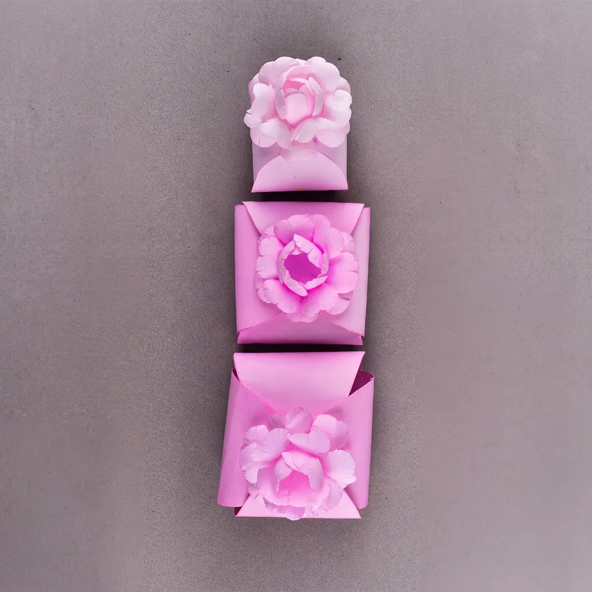 Três caixinhas cartonadas rosa da Embalarte com flor de papel no topo, em tamanhos diferentes